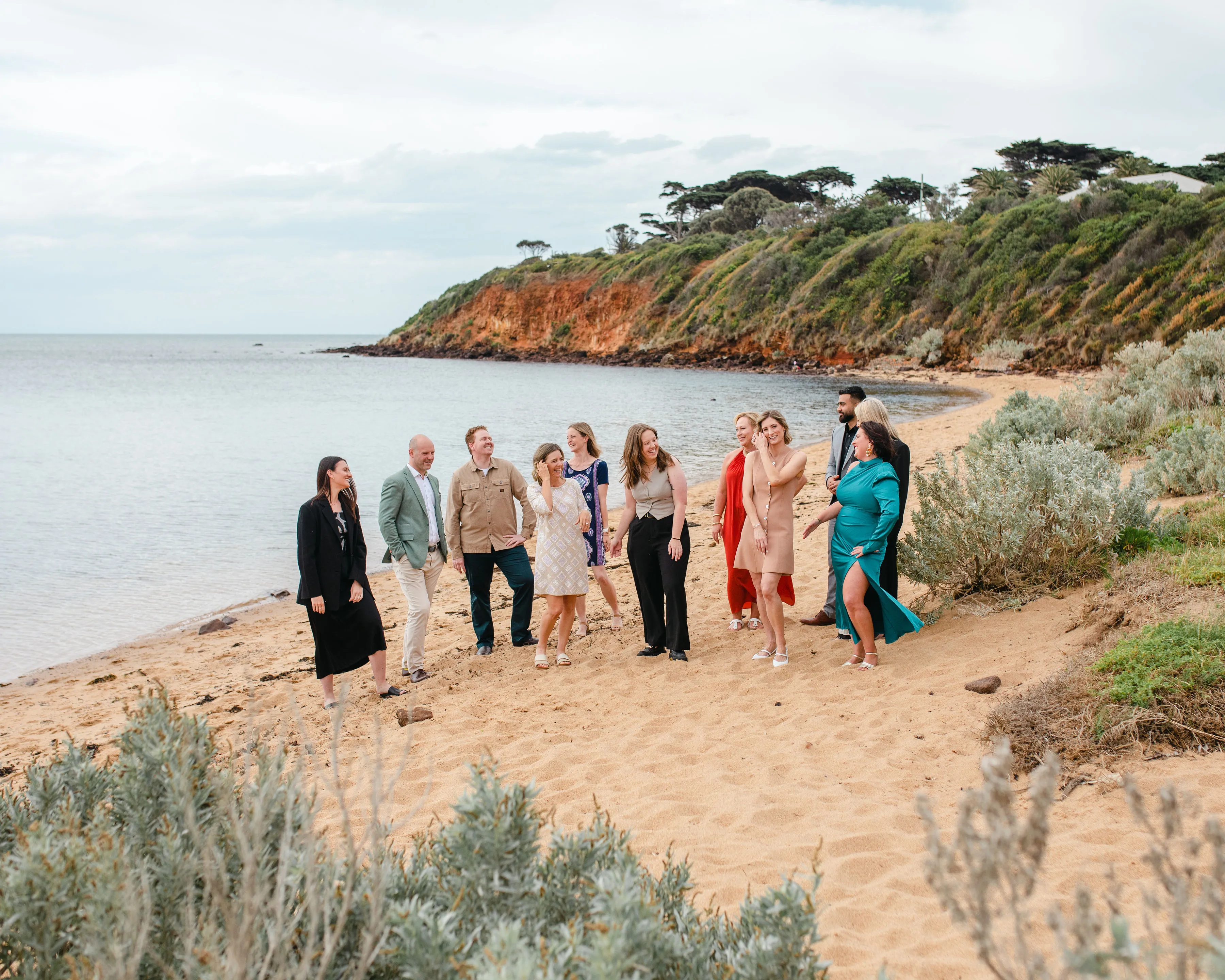 PIER team standing and chatting on a sandy beach with greenery and rocky cliffs in the background.