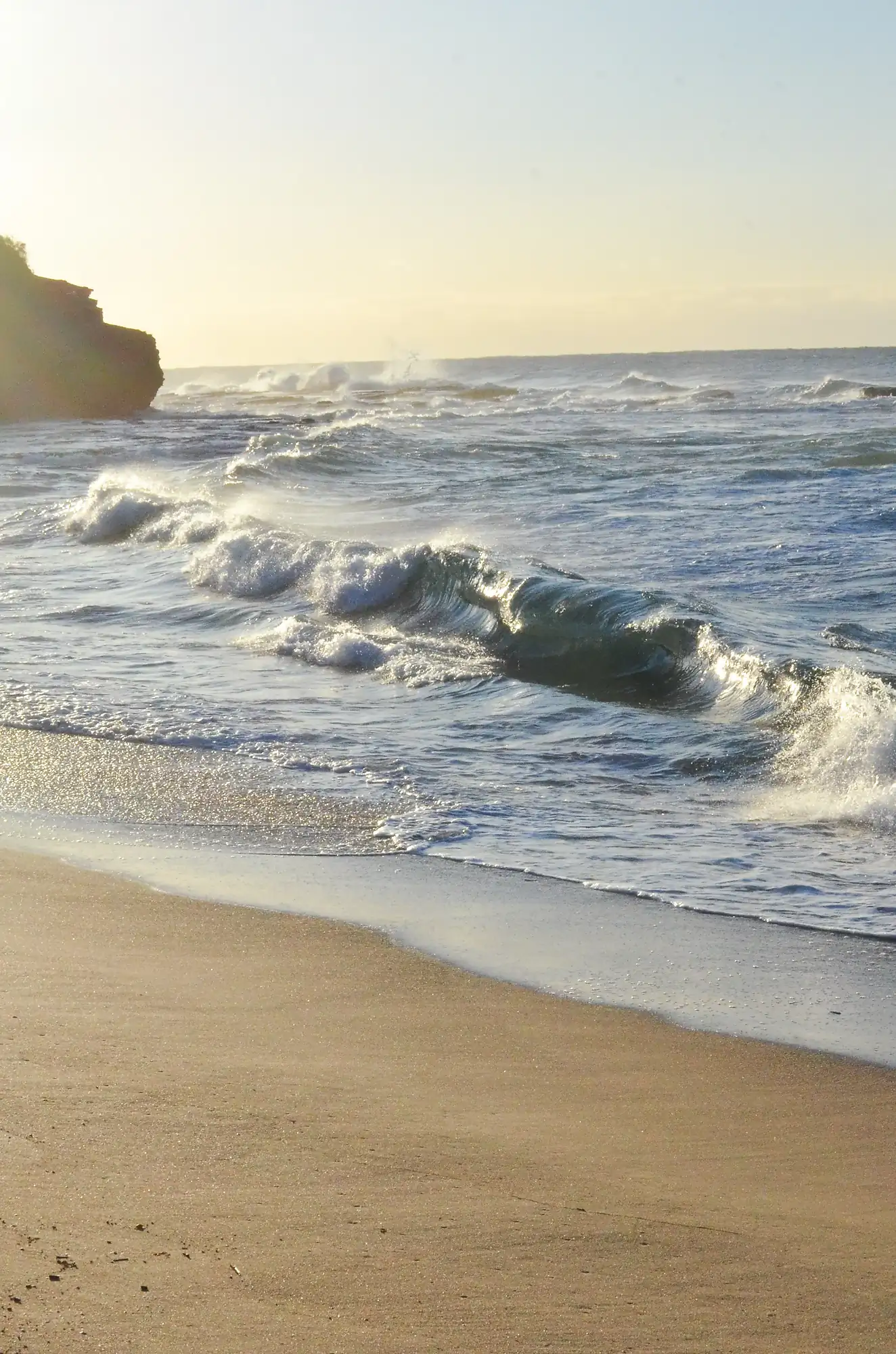 Gentle ocean waves rolling onto a sandy beach during a calm, sunlit evening.