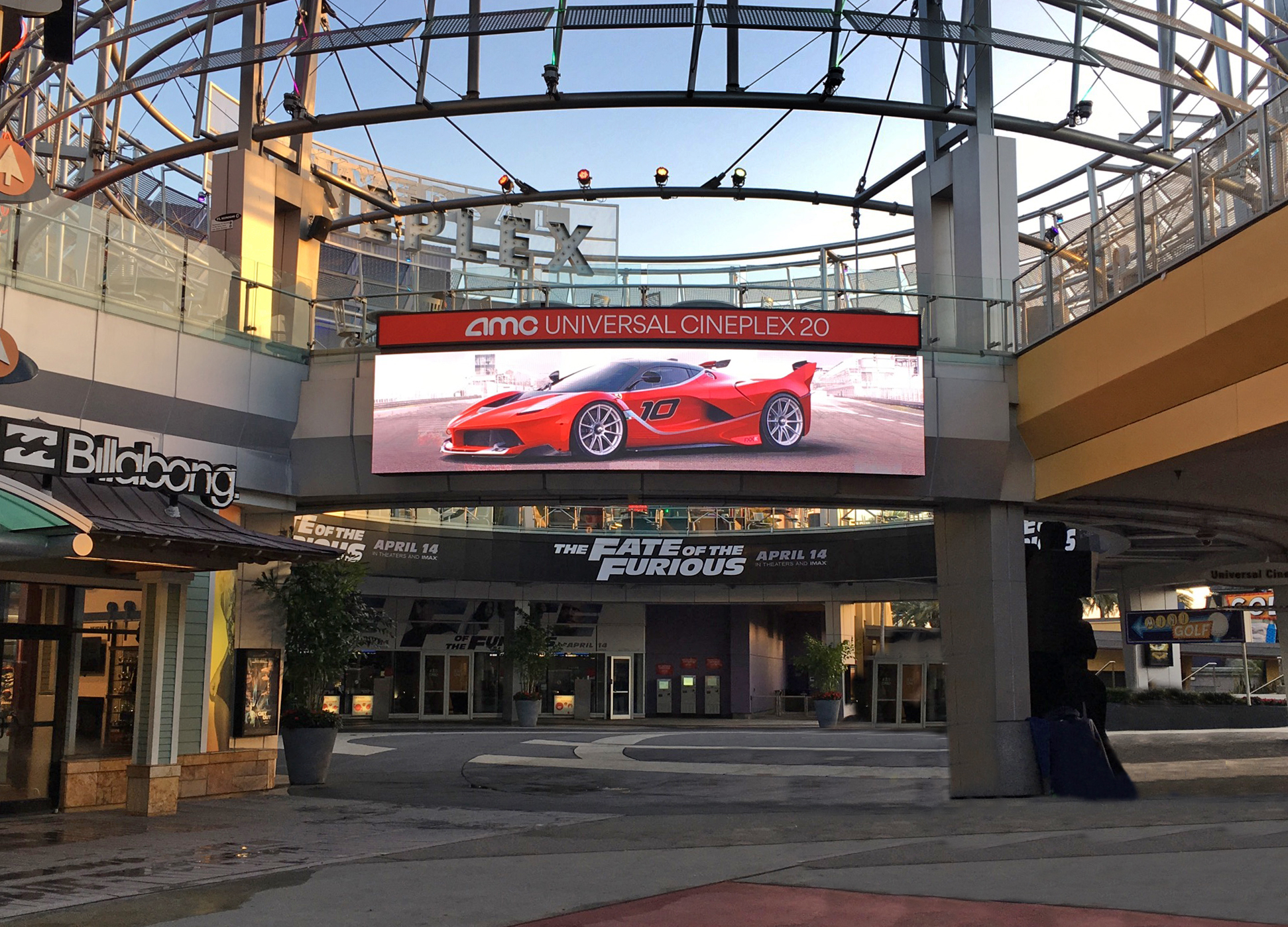 Entrance to AMC Universal Cineplex 20 with a large digital billboard displaying a red sports car and a banner promoting The Fate of the Furious movie.