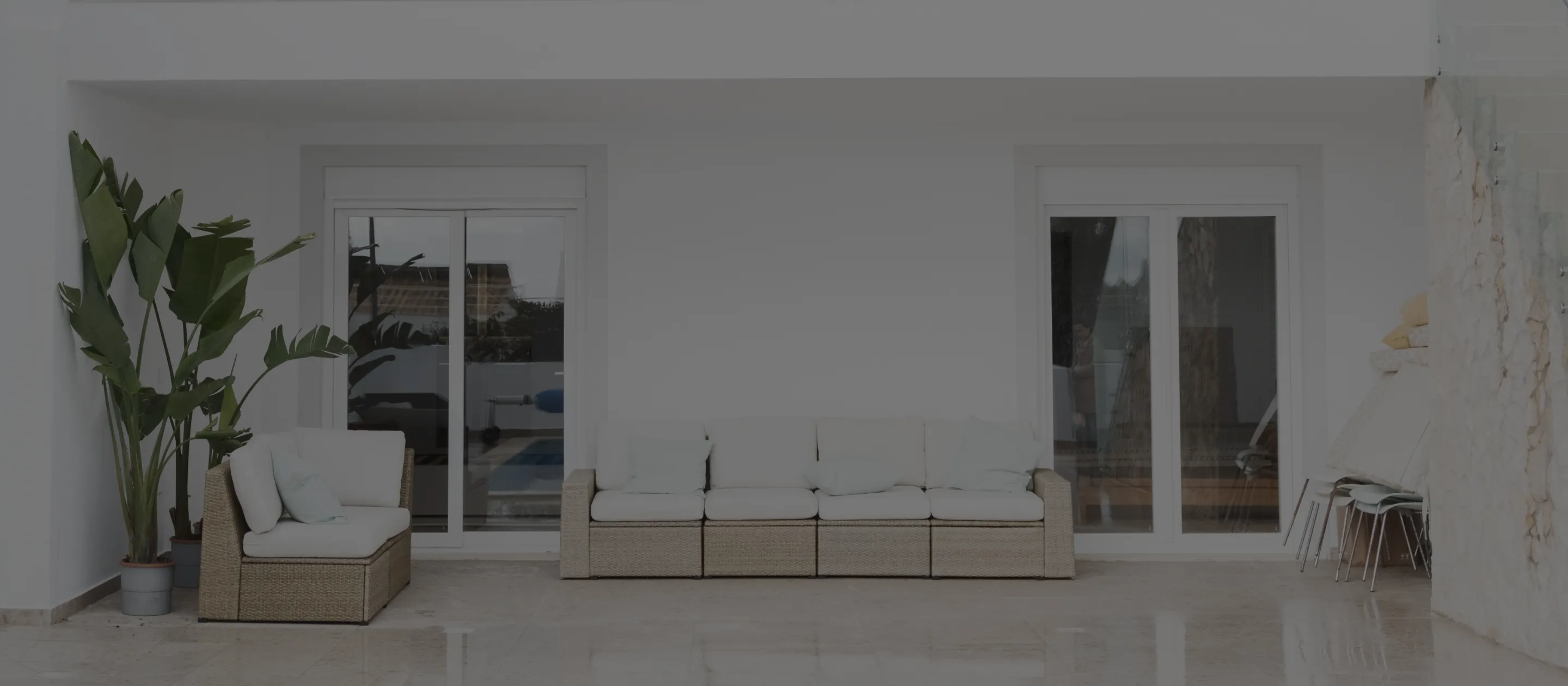 Minimalist outdoor patio with wicker sofas, potted plants, and sliding glass doors.