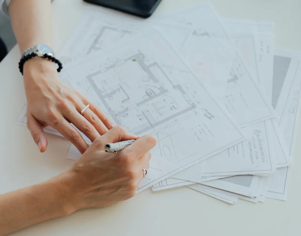 Close-up of architect’s hands sketching over building blueprints during a property planning session.