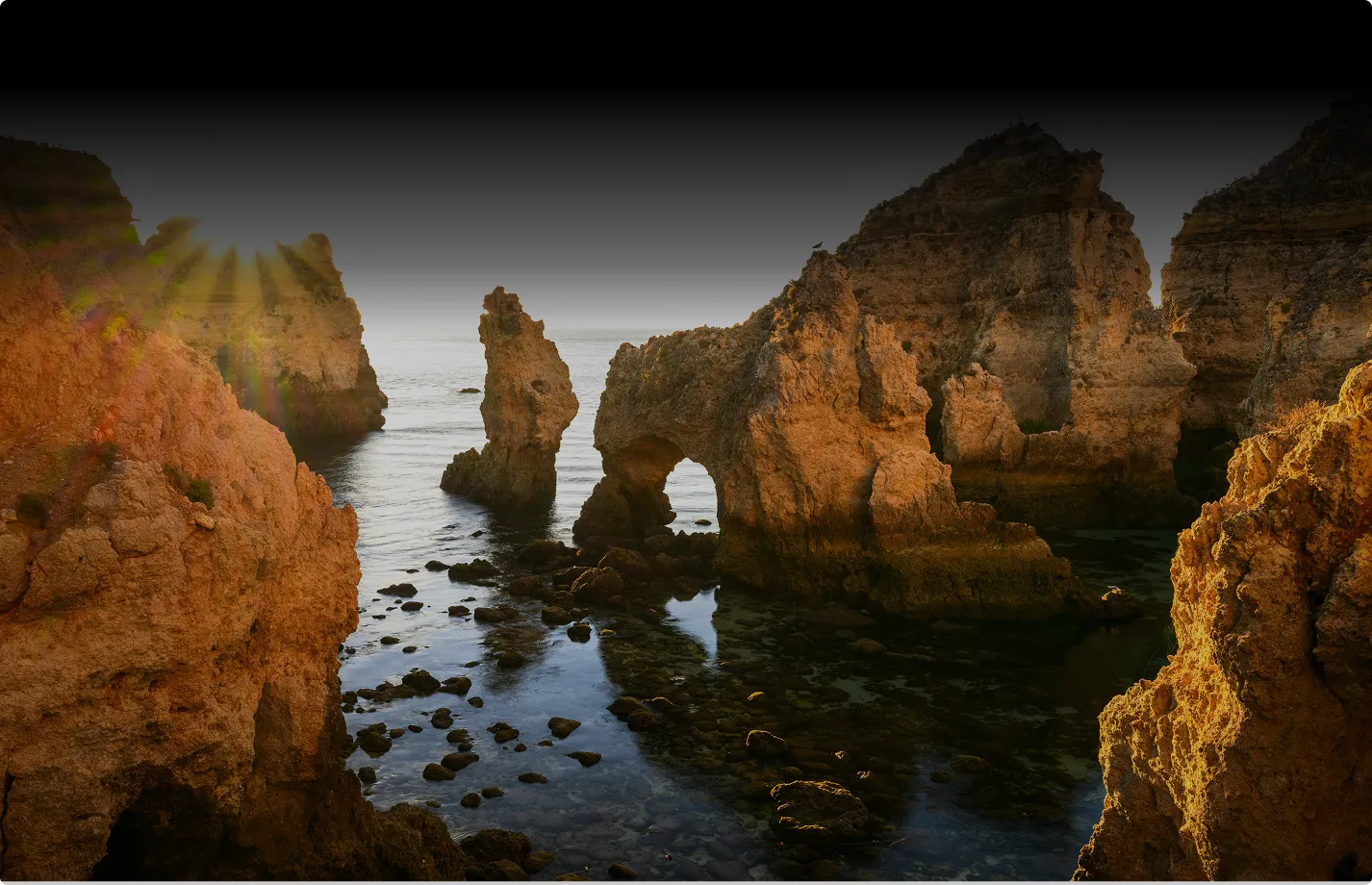 Scenic view of golden rock formations and sea caves along the Algarve coastline at sunset.