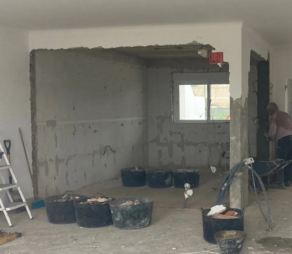 Old apartment hallway with visible wall damage, wooden parquet flooring, and doors leading to different rooms.