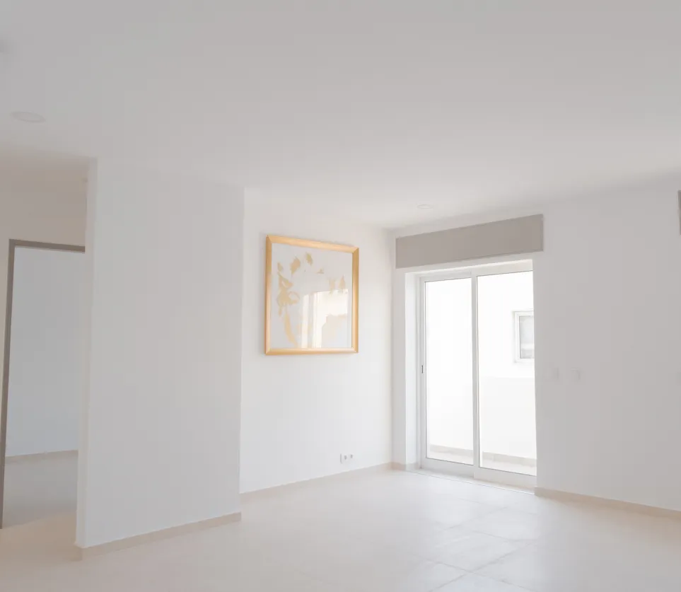Minimalist renovated living room with white walls, sliding glass doors, and natural light.