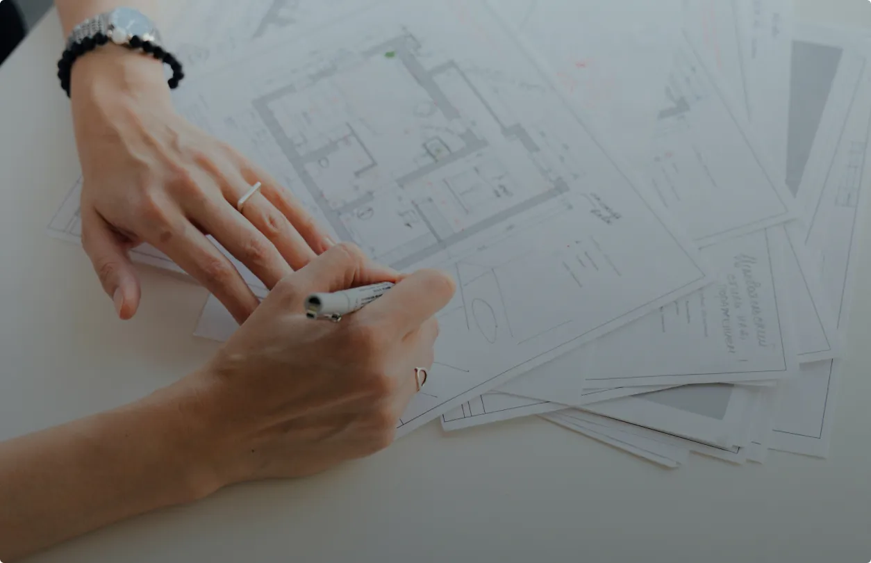 Close-up of architect’s hands sketching over building blueprints during a property planning session.