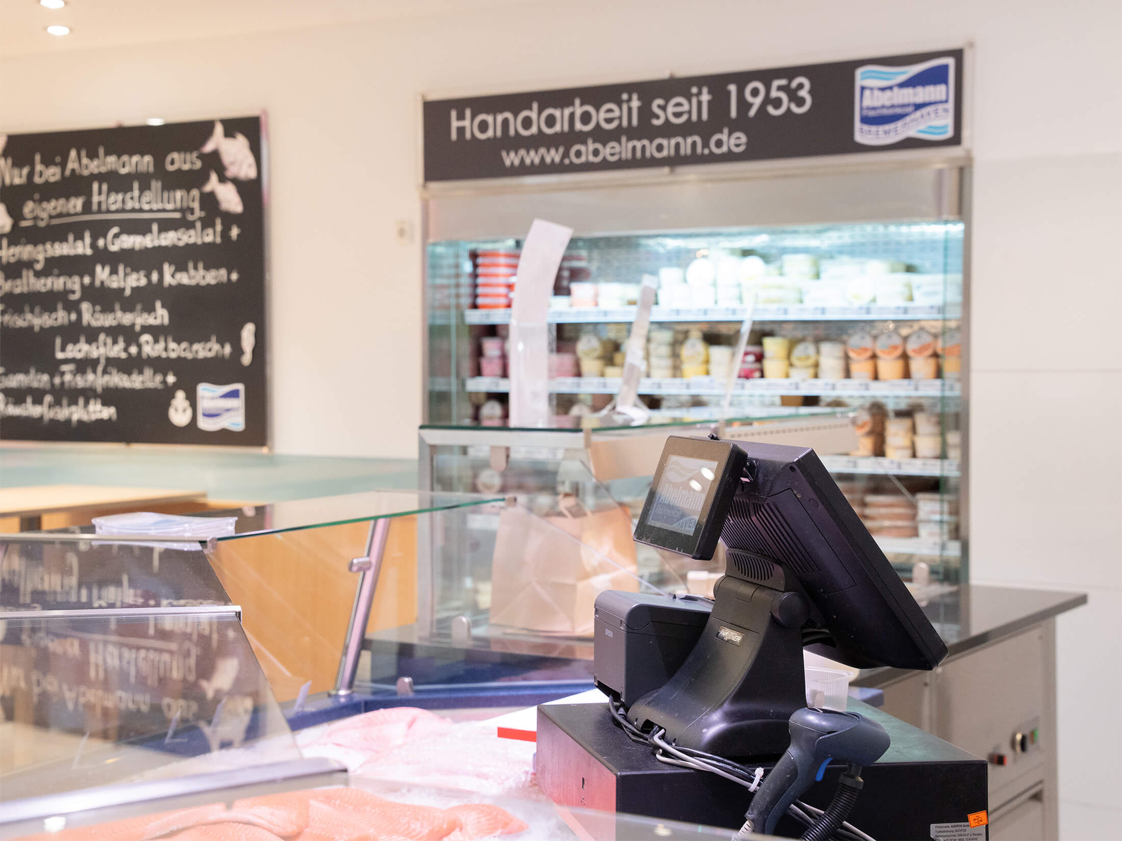 Kasse und Regal mit hausgemachten Feinkostprodukten im Abelmann-Fachgeschäft mit Hinweis auf Tradition seit 1953.