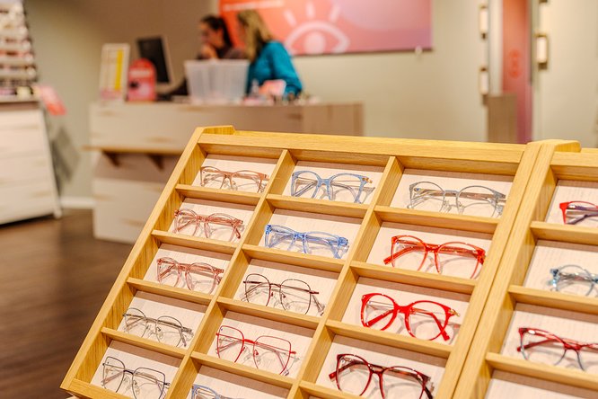 Farbige Brillenfassungen in einer Holzpräsentation im Verkaufsraum von eyes + more.