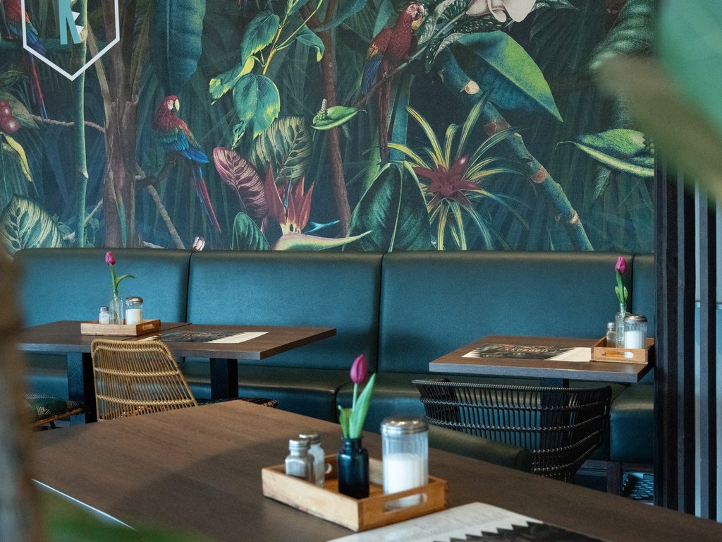 Mehrere Tische mit Tischdeko und floraler Wandgestaltung im Hintergrund des Krokodil-Restaurants.