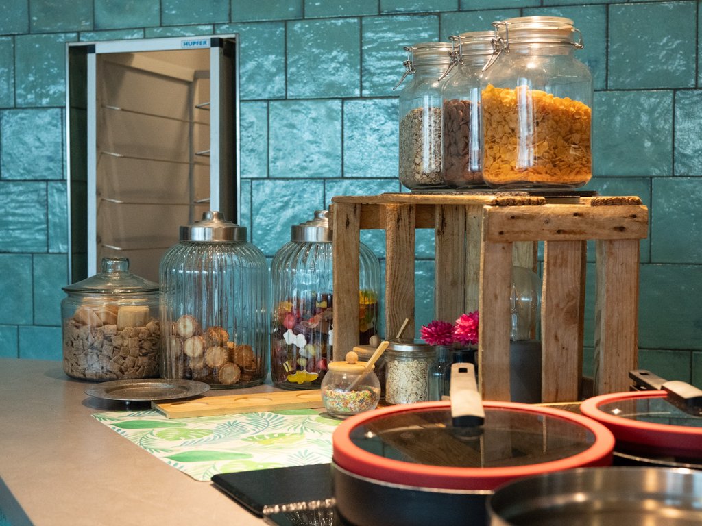 Frühstücksbar im Krokodil mit Gläsern voller Cerealien, Toppings und Snacks vor türkisfarbener Kachelwand.