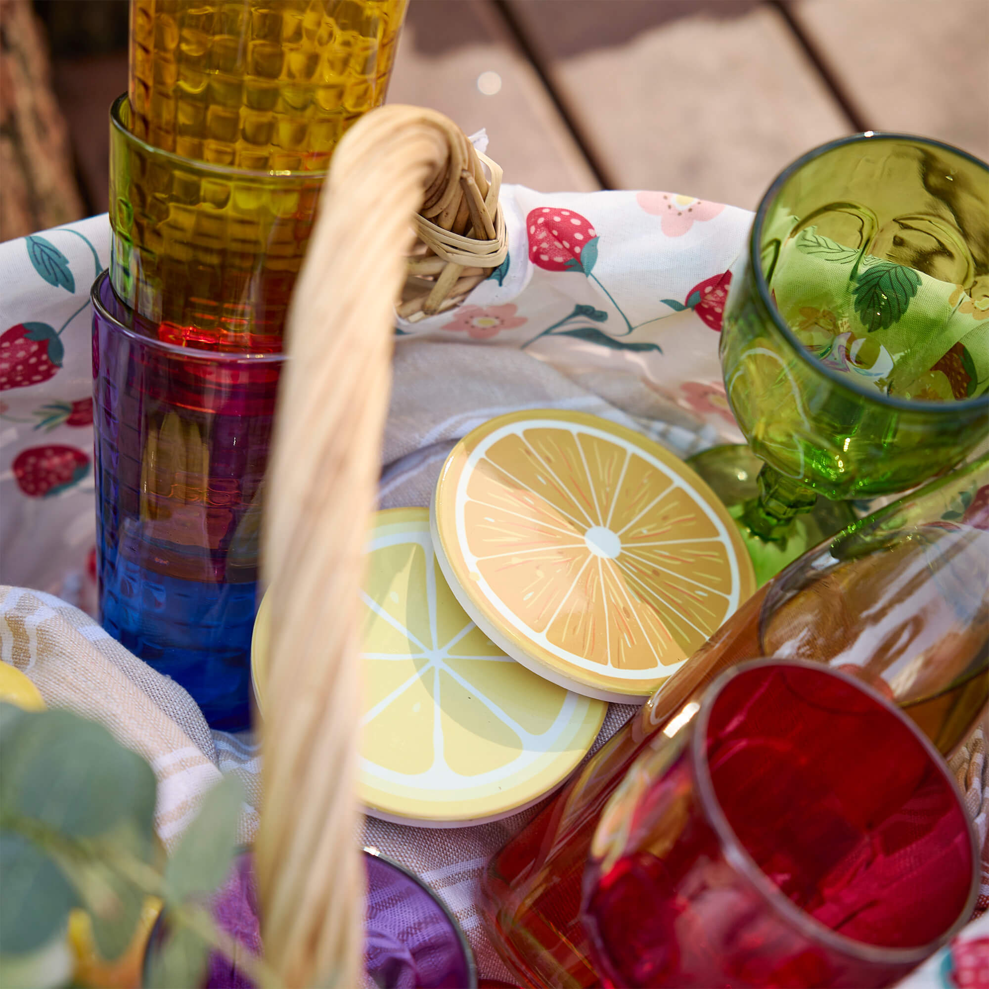 Bunte Gläser und Zitronenuntersetzer in einem Picknickkorb mit Erdbeerstoff