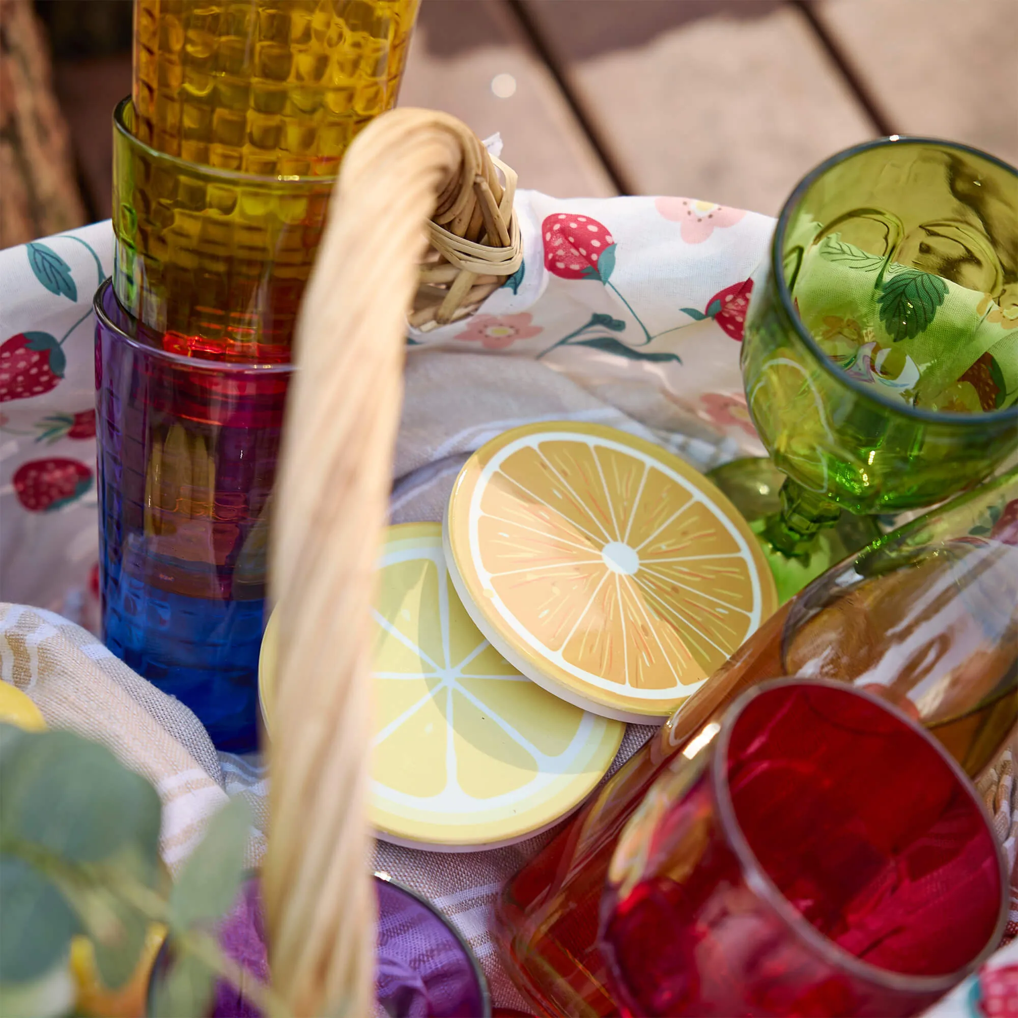 Bunte Gläser und Zitronenuntersetzer in einem Picknickkorb mit Erdbeerstoff
