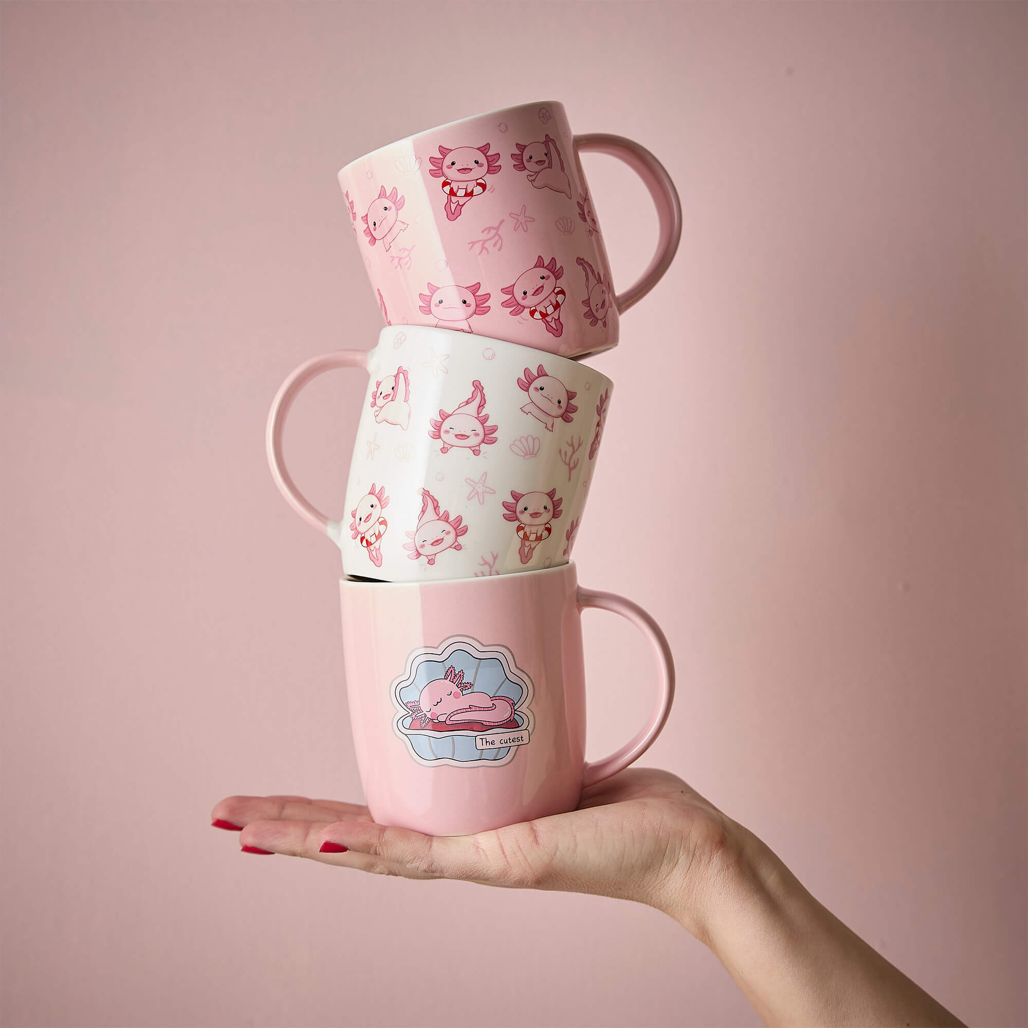 Drei rosa Tassen mit süßen Axolotl-Motiven auf einer Hand balanciert
