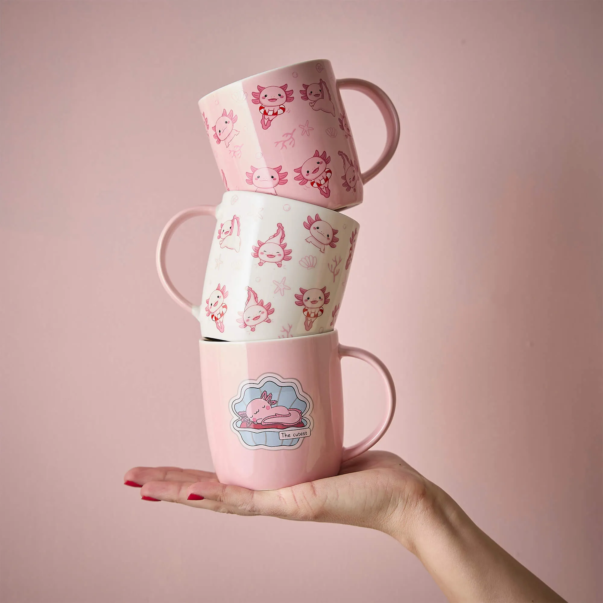 Drei rosa Tassen mit süßen Axolotl-Motiven auf einer Hand balanciert
