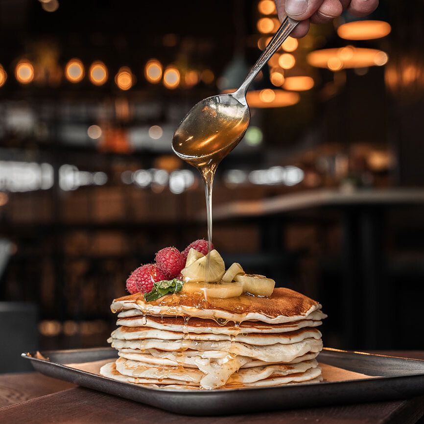 Frisch zubereitete Pancakes mit Honig, Banane und Himbeeren – ein süßer Start in den Tag