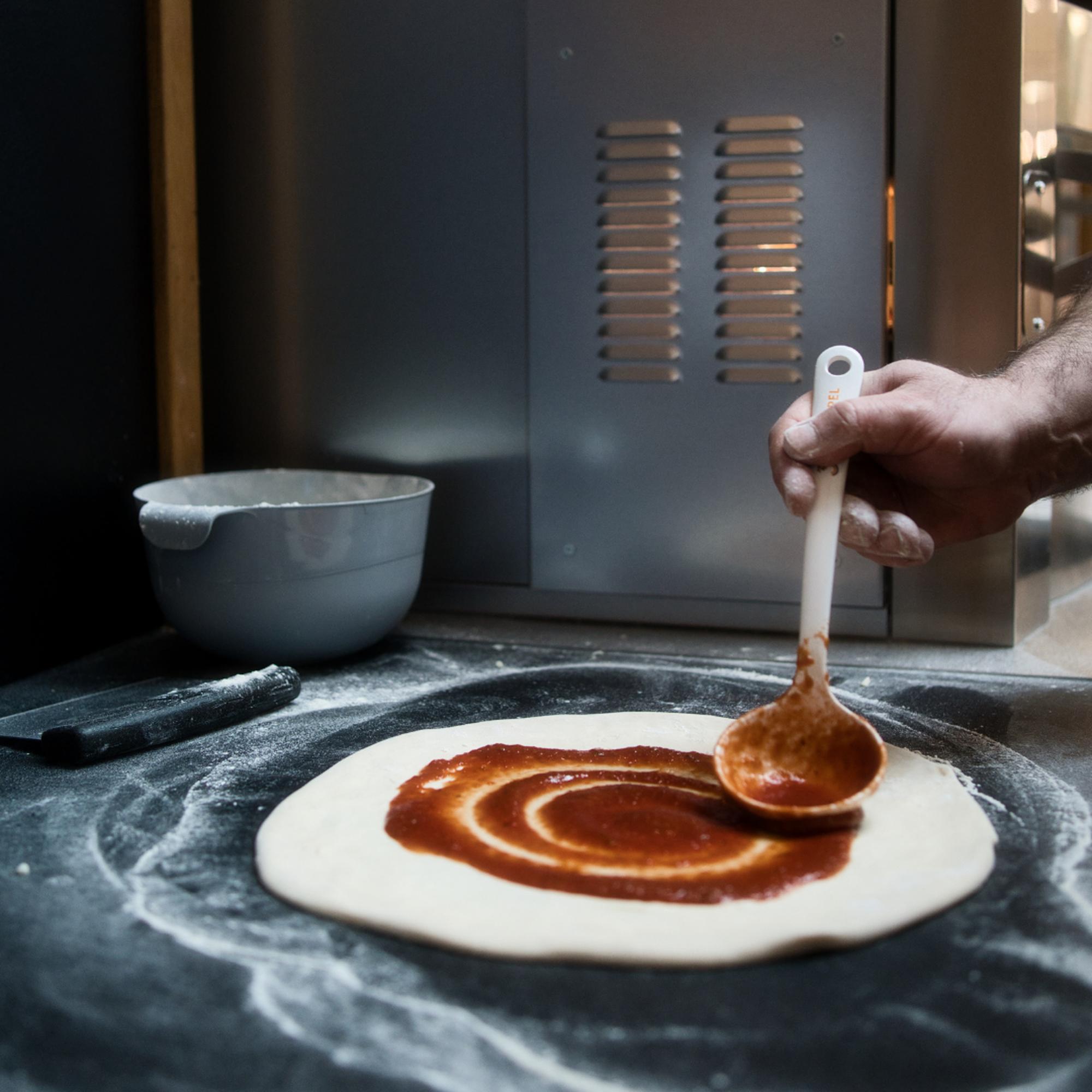 Frischer Pizzateig wird im Eiscafé & Restaurant Rimini mit Tomatensauce bestrichen.