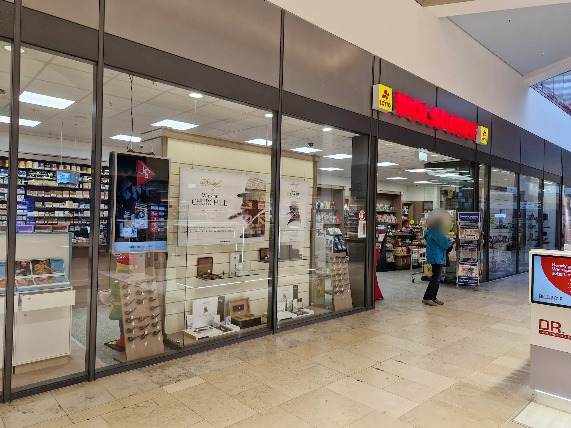 Eingang der WOLSDORFF-Filiale mit rotem Logo und breitem Einblick ins Geschäft mit Tabakwaren, Presseartikeln und Lottoangebot.