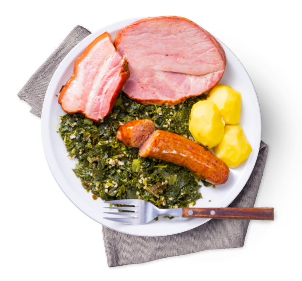 Auf einem weißen Teller ist eine Portion Grünkohl mit Kartoffeln, Wurst und Kassler angerichtet.