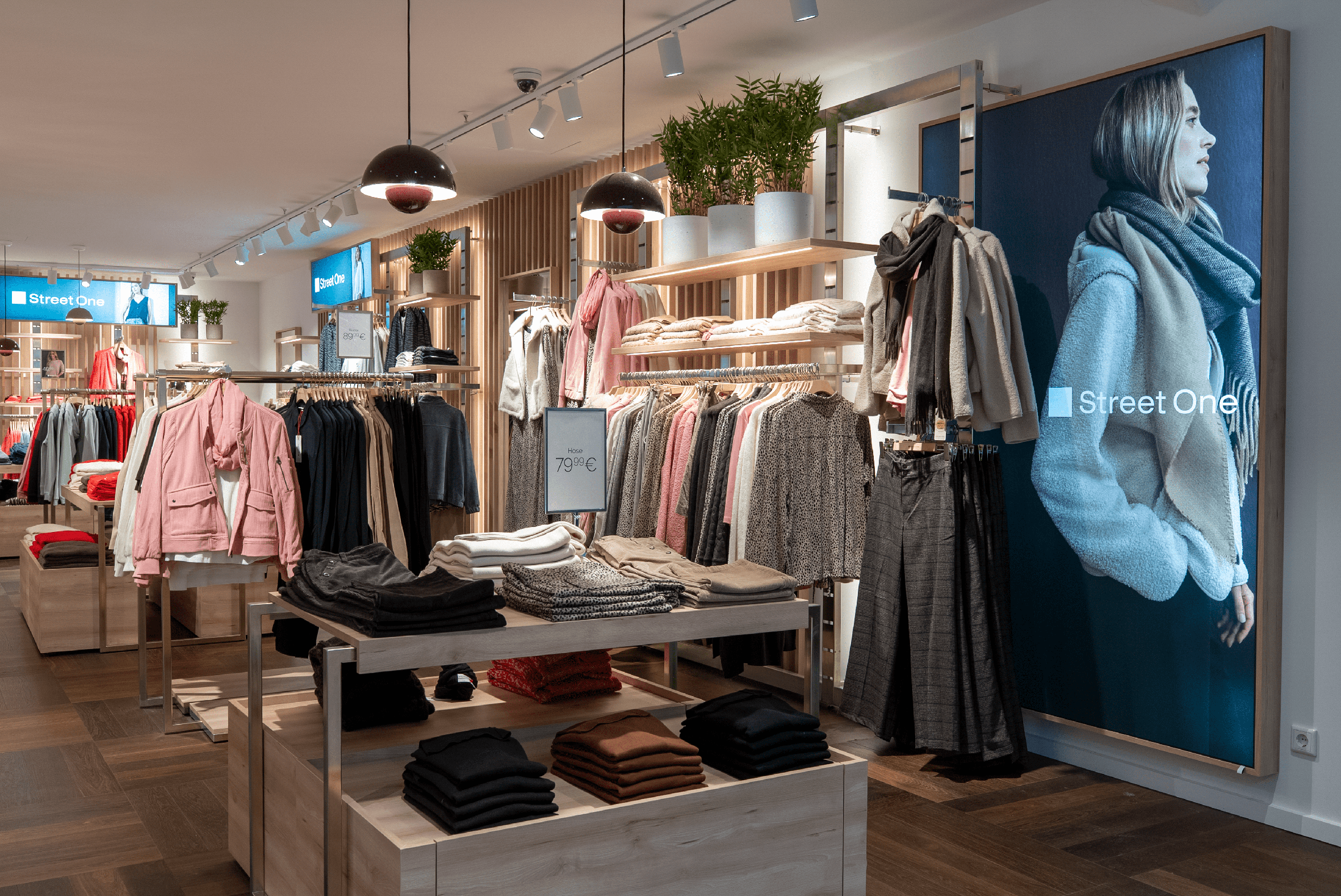 Ein freundlicher Innenraum von Street One mit verschiedenen bestückten Regalen und Tischen mit Kleidung.