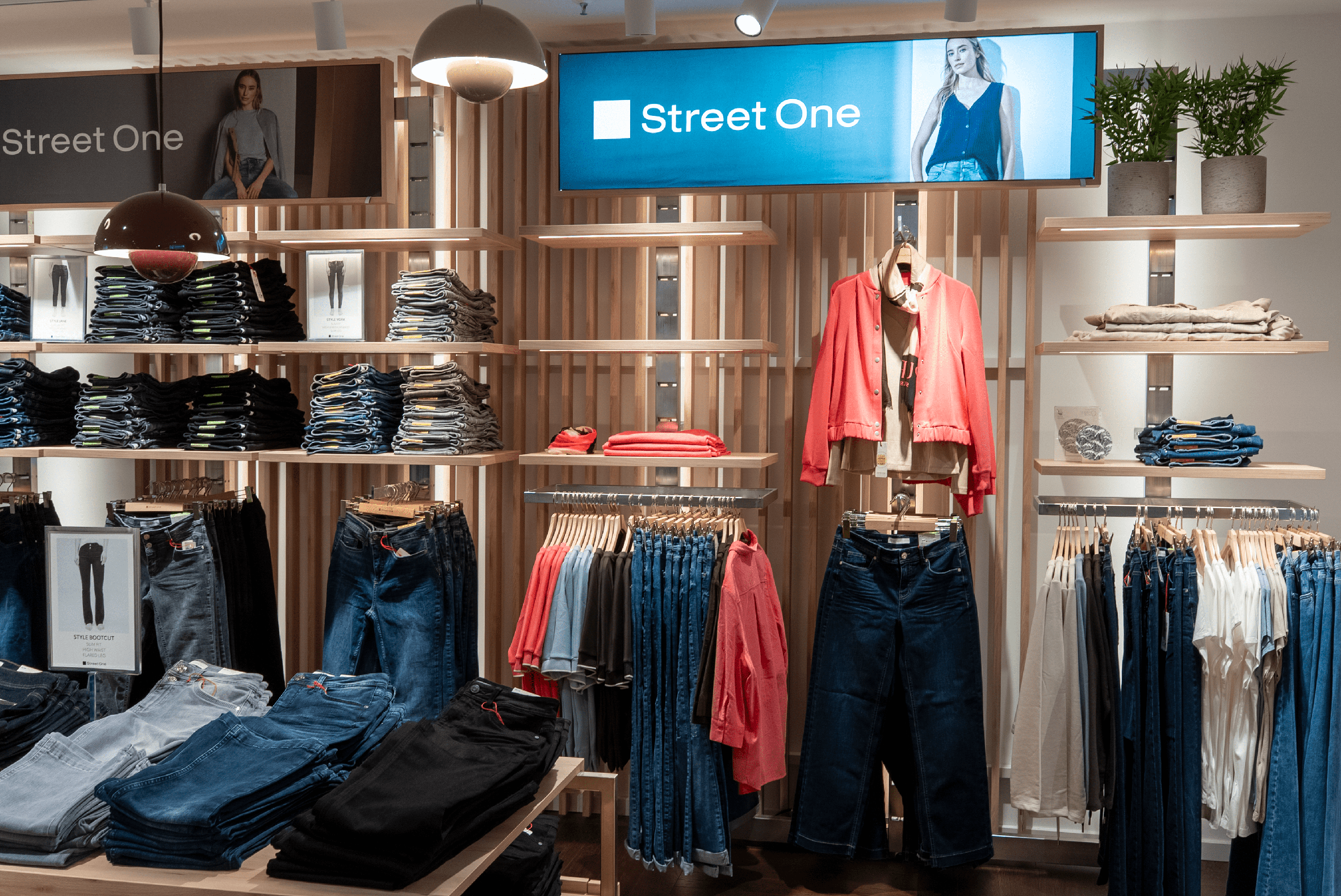 Der Innenraum vom Street One Store zeigt Jeans gestapelt im Regal und auf einem Tresen, sowie einige roten Jacken am Haken.