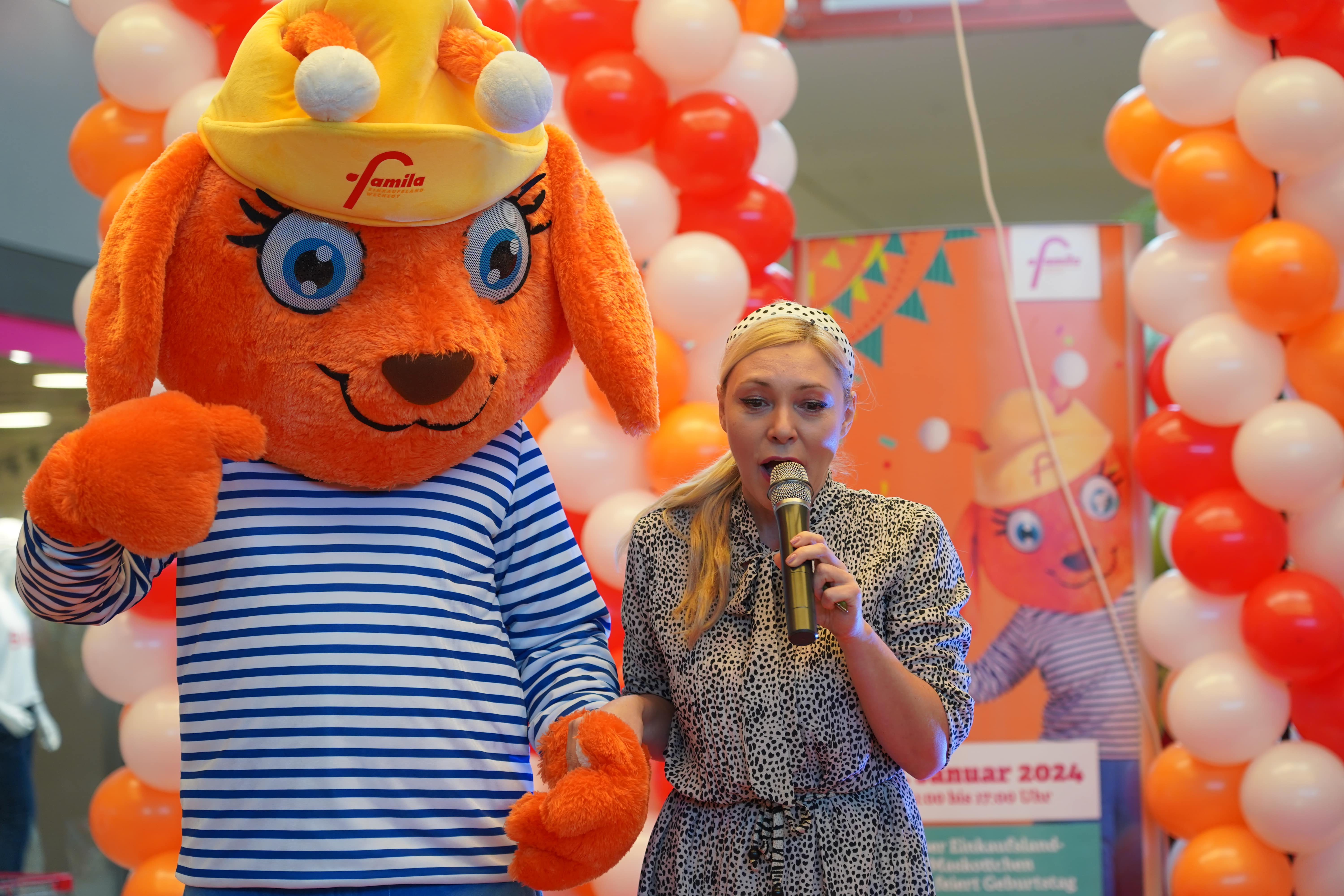 Luna steht mit einer Moderatorin auf der Bühne vor Luftballons und begrüßt ihre Gäste.