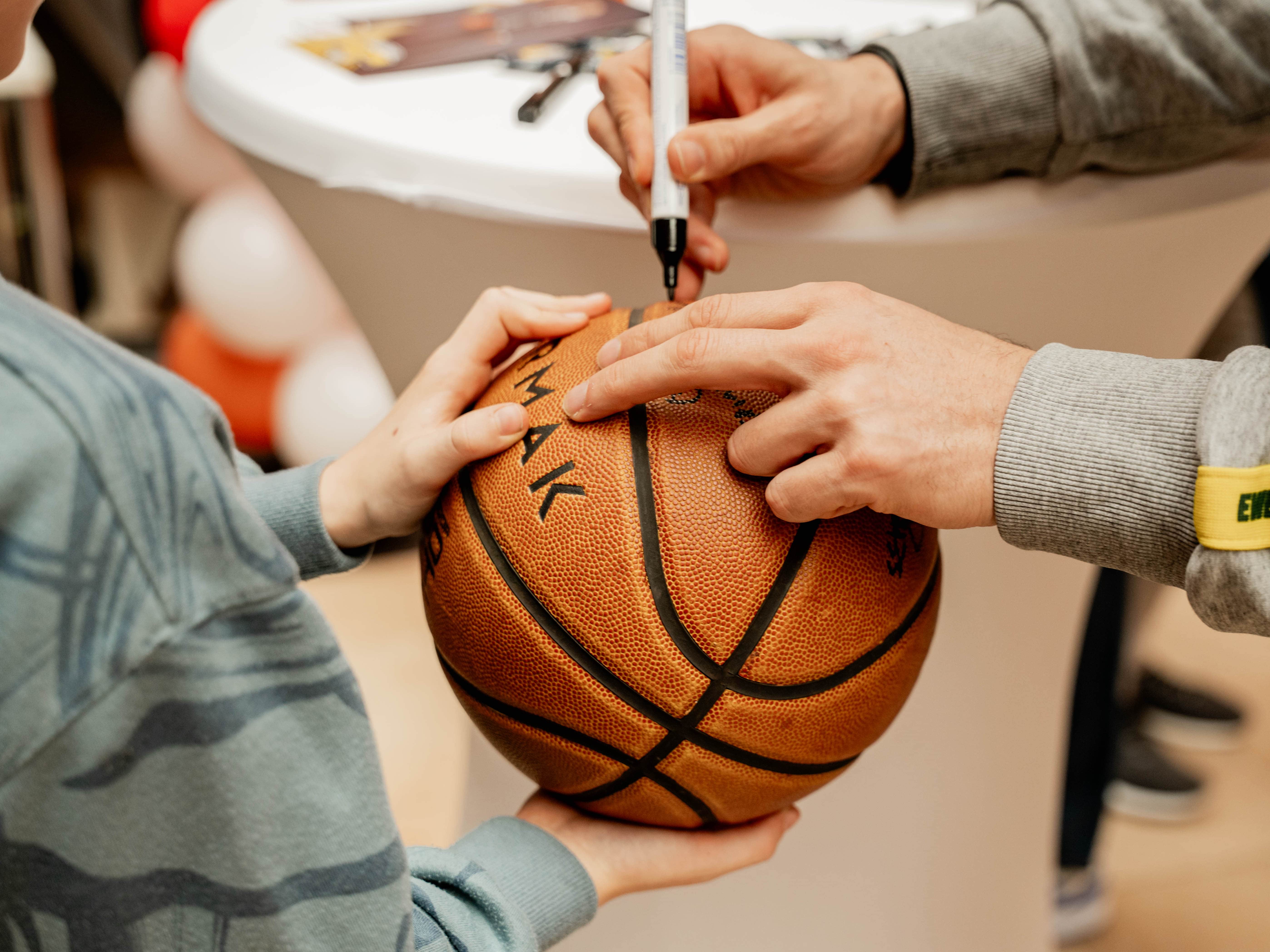 Ein Kind lässt einen Basketball von einem Spieler der EWE Baskets Oldenburg mit einem Edding unterzeichnen.
