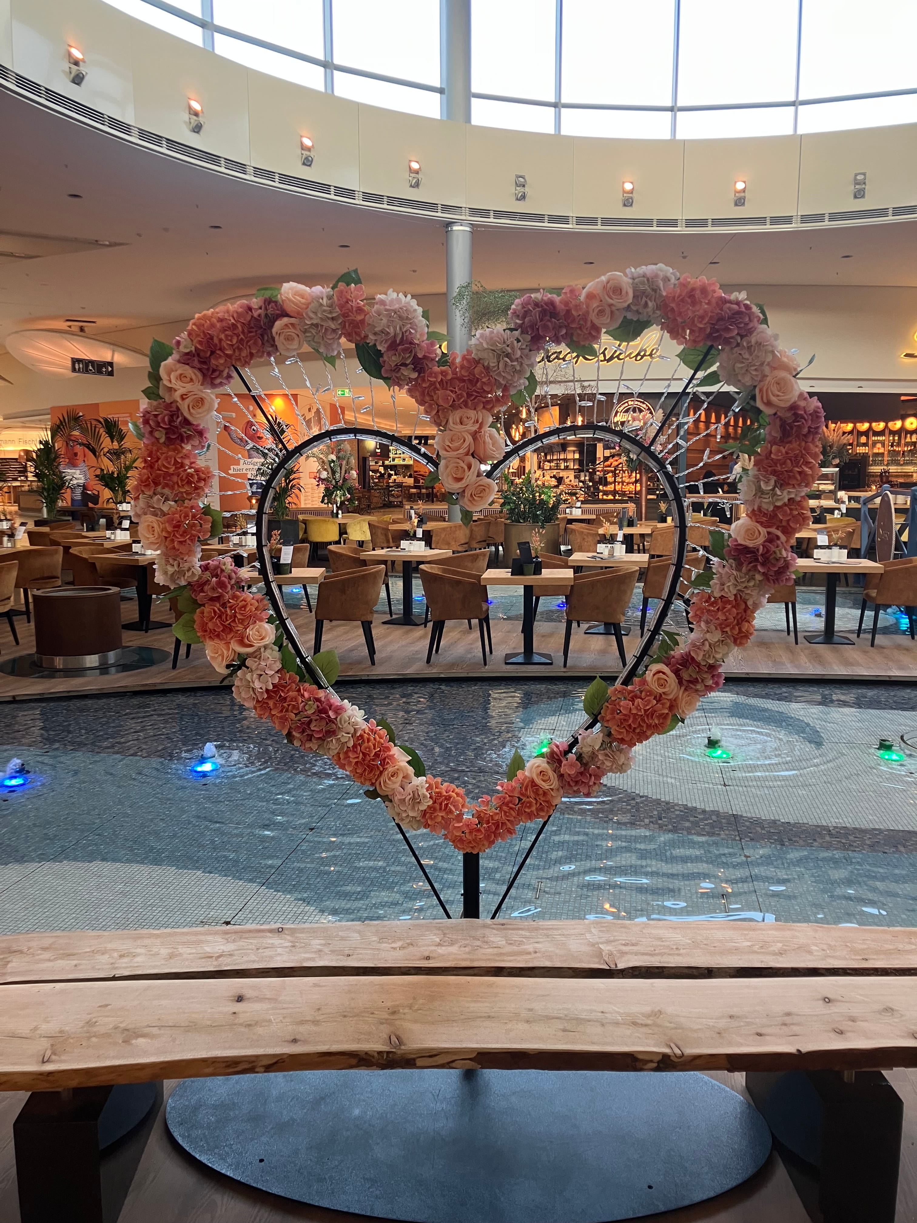 Ein geschmücktes Herz mit Beleuchtung steht vor dem Brunnen im Einkaufsland.