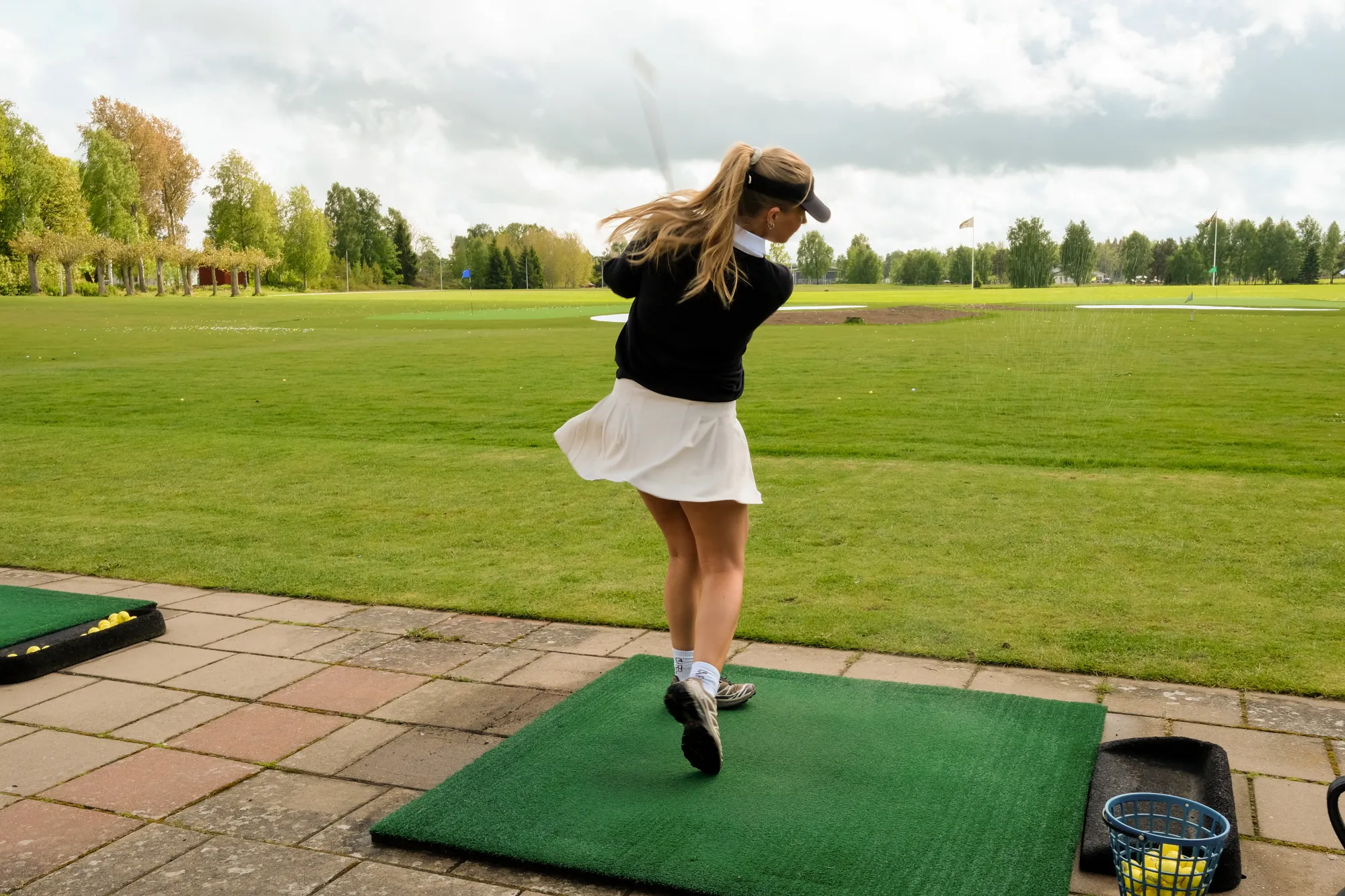 Tjej som slår golfboll på driving range utomhus