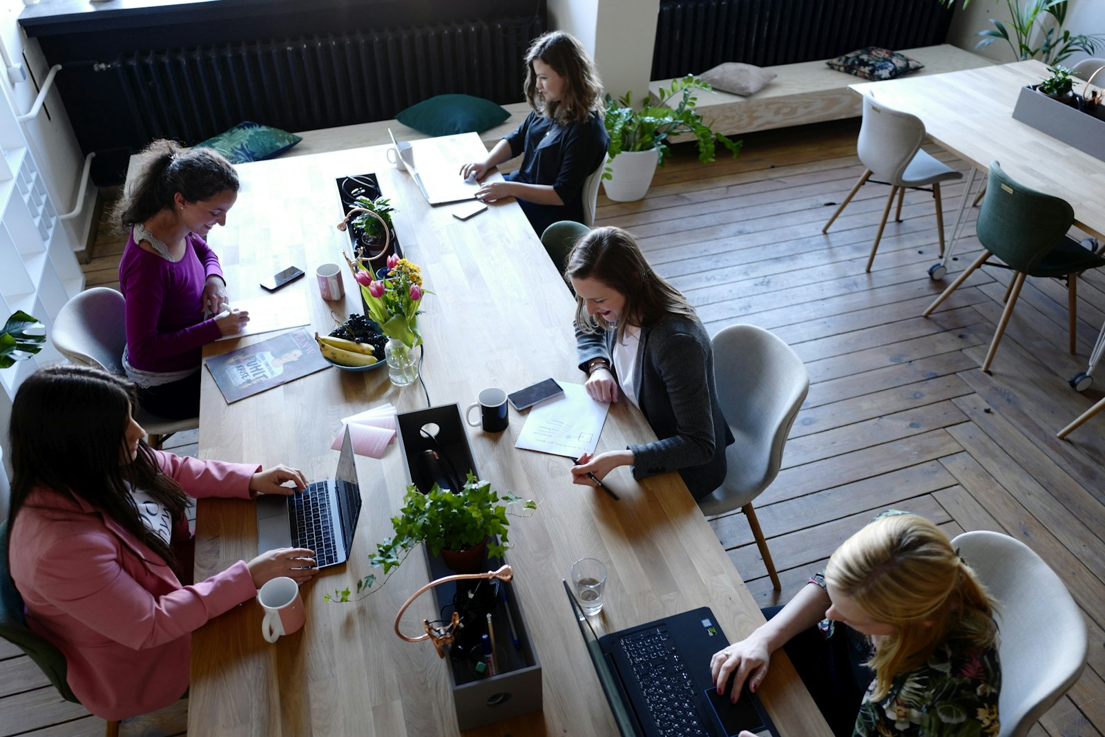 Plusieurs personnes travaillant côte à côte autour d'une grande table en bois dans un espace de travail partagé