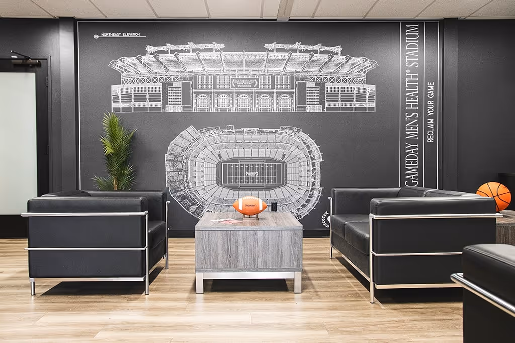 Interior of a Gameday Men’s Health clinic featuring a sleek waiting area with leather chairs, a football-themed mural, and sports décor designed for a comfortable, male-focused experience.