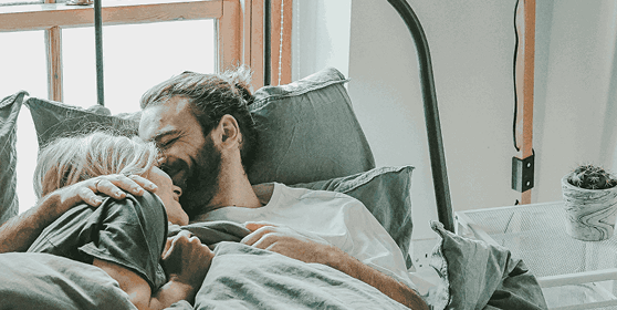 Smiling couple embracing in bed, reflecting the emotional and physical benefits of effective erectile dysfunction treatment offered by Gameday Men’s Health.