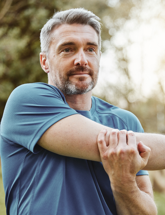 Confident middle-aged man stretching outdoors, symbolizing strength, health, and proactive care offered at Gameday Men’s Health.