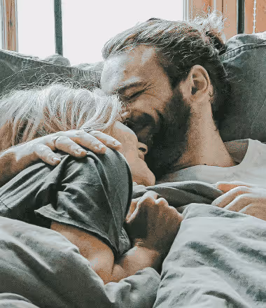Smiling couple embracing in bed, reflecting the emotional and physical benefits of effective erectile dysfunction treatment offered by Gameday Men’s Health.