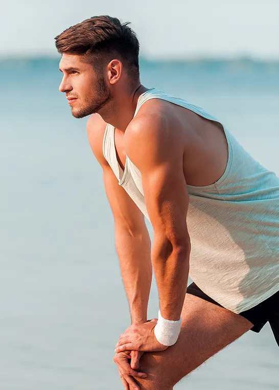 Fit man resting after outdoor workout by the water, representing energy, recovery, and vitality supported by men’s vitamin injection therapy.