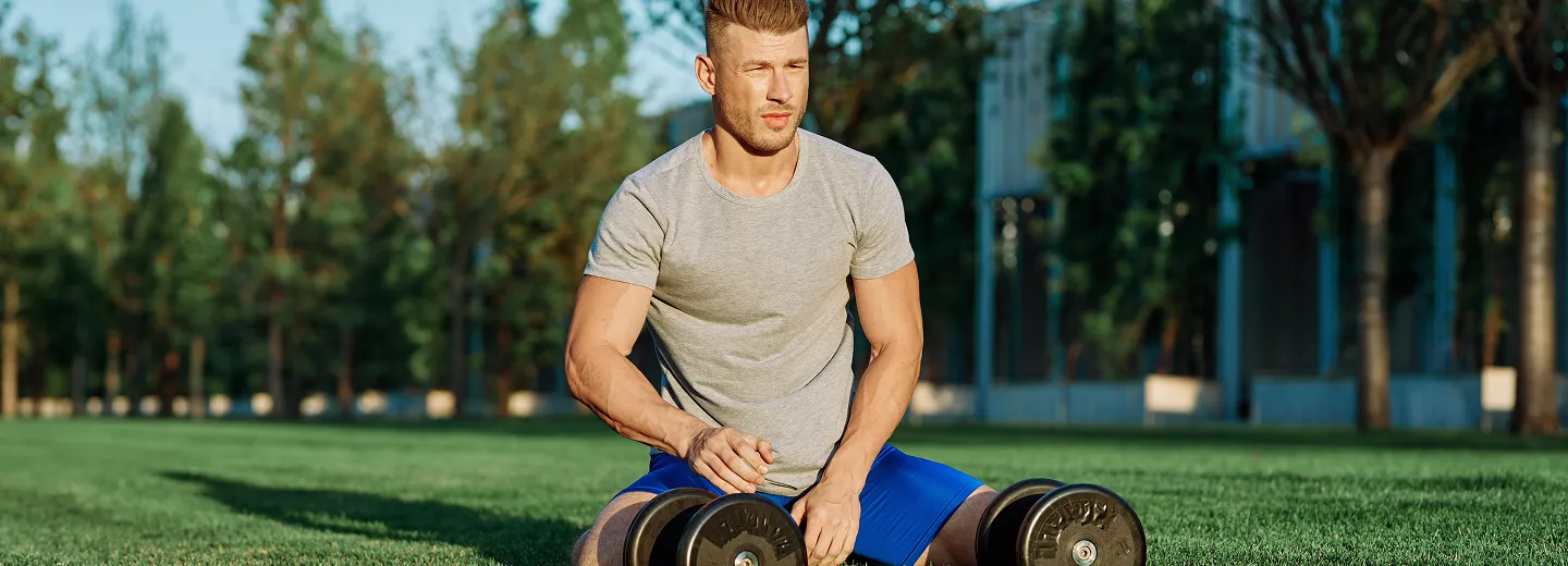 Man resting on grass next to dumbbells, representing enhanced endurance, muscle recovery, and immune health from Vitamin C injections. 