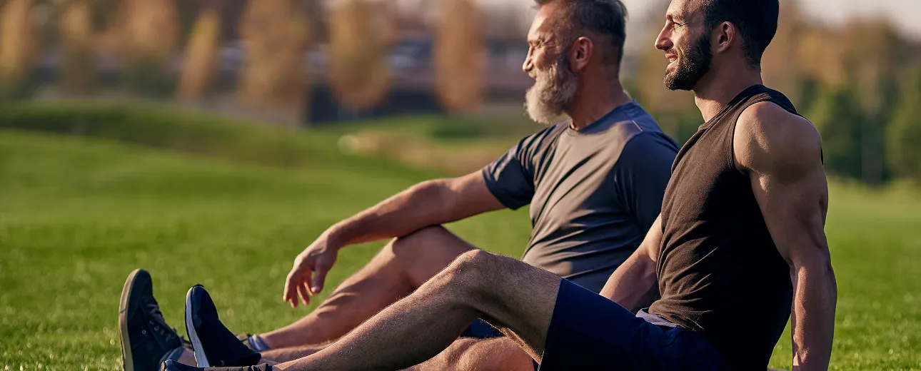 Two men sitting on grass post-workout, symbolizing restored energy, focus, and connection through oral testosterone treatment. 