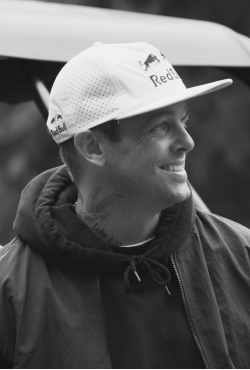 Black and white image of professional skateboarder Ryan Sheckler smiling in a hoodie and Red Bull cap, featured as a Gameday Men's Health influencer.