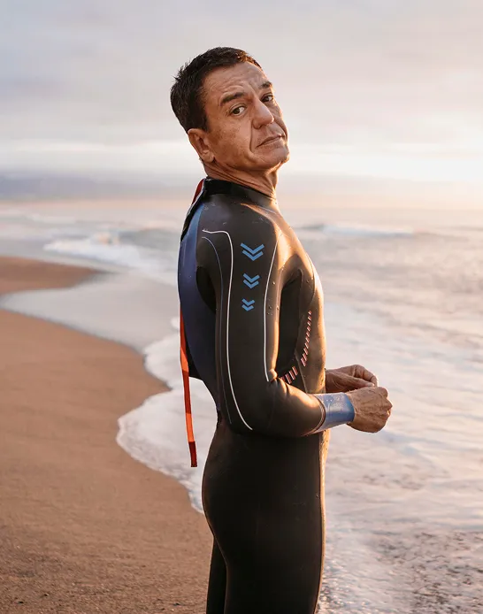 Confident middle-aged man in a wetsuit standing on the beach, symbolizing vitality and wellness supported by testosterone therapy.