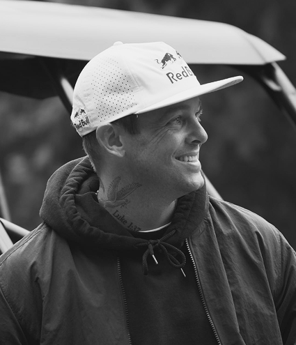 Black and white image of professional skateboarder Ryan Sheckler smiling in a hoodie and Red Bull cap, featured as a Gameday Men's Health influencer.