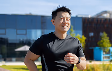 asian smiling young man dressed sportswear is doing morning jog park near lake
