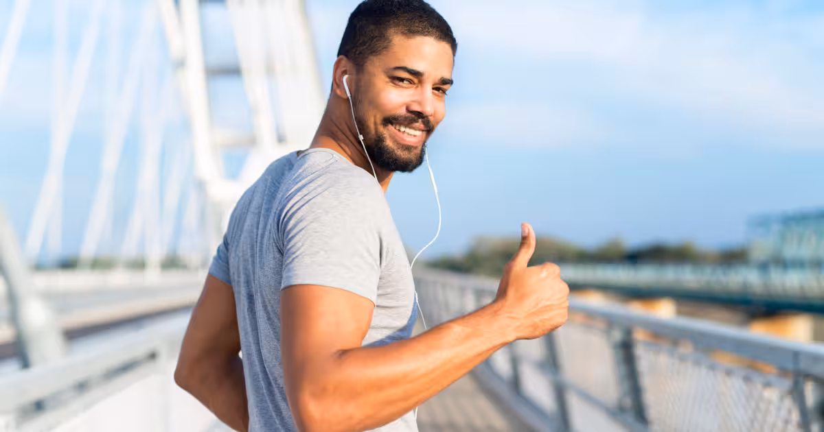A man on a bridge, showing a thumbs-up, feeling energized and rejuvenated thanks to HGH therapy.