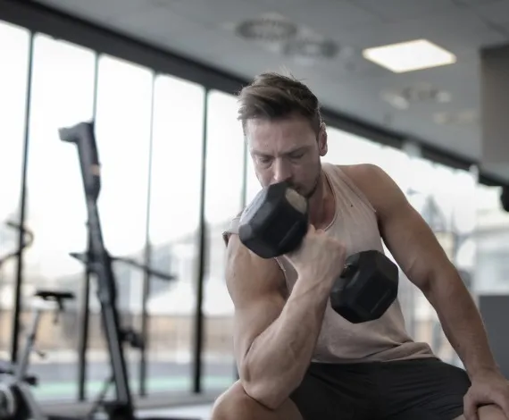 Man lifting dumbbells in the gym, incorporating strength training to support muscle growth along with Sarcotropin IPA