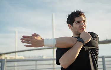 Young man stretching outdoors near a bridge, representing enhanced recovery, antioxidant protection, and immune health supported by glutathione injections.