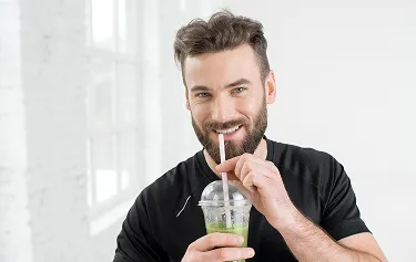  Smiling man in athletic wear drinking a green smoothie, representing healthy lifestyle and liver support from MIC lipotropic injections. 