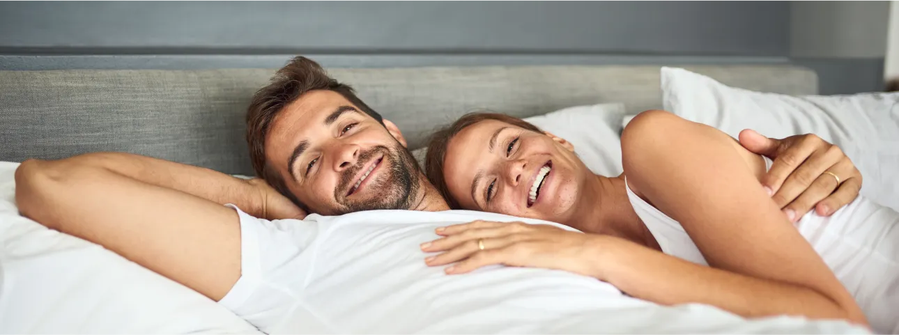 Happy couple relaxing in bed, symbolizing improved energy and intimacy from oral testosterone therapy.