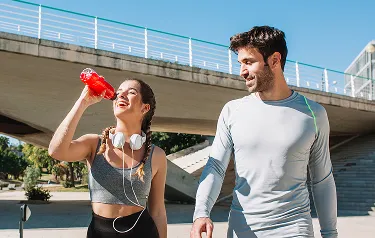 Man and woman walking outdoors after exercise, woman drinking from bottle, representing hydration, energy, and wellness benefits from vitamin injections.
