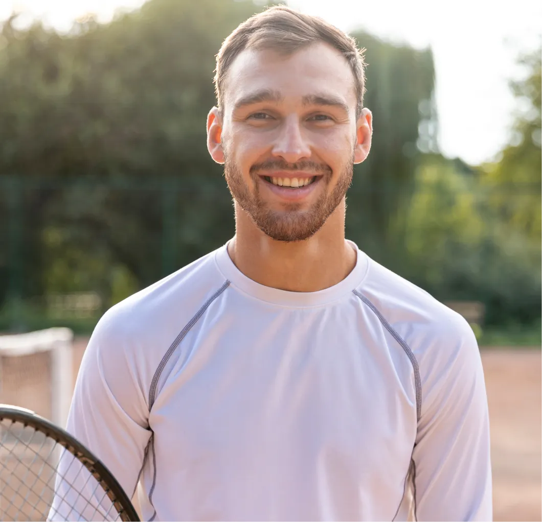 Smiling man holding a tennis racket on the court, reflecting the immune support and antioxidant benefits of Vitamin C injections for active men.