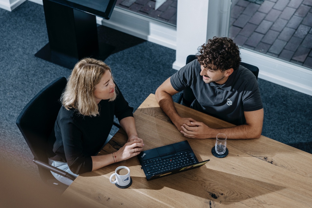 Zwei Kolleg:innen diskutieren an einem Laptop.
