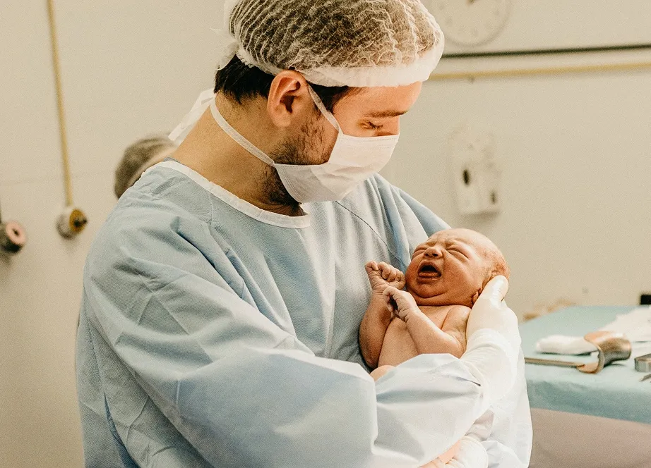 A man in a hospital gown holding a baby.