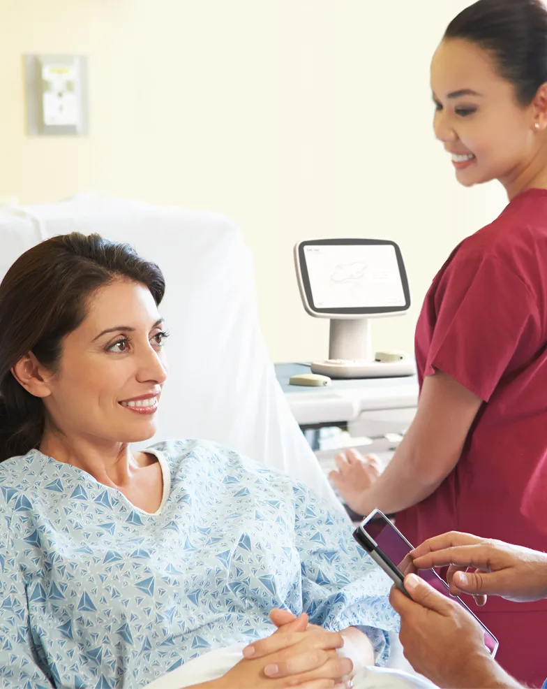 A woman in a hospital bed talking to a nurse.