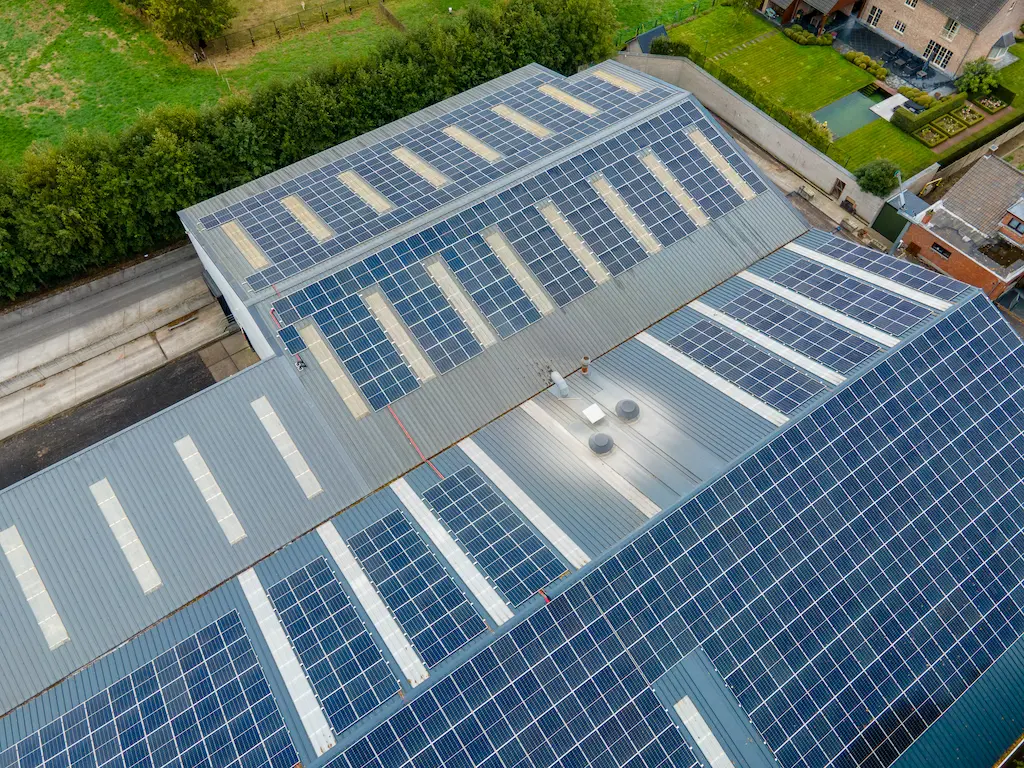 Luchtfoto van een grootschalige installatie van zonnepanelen door Energy Protect op het hellende metalen dak van een bedrijfsgebouw, inclusief strategische plaatsing rondom lichtkoepels.